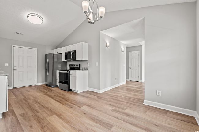 Kitchen featuring appliances with stainless steel finishes, white cabinets, light wood finished floors, vaulted ceiling, and a chandelier | Image 11
