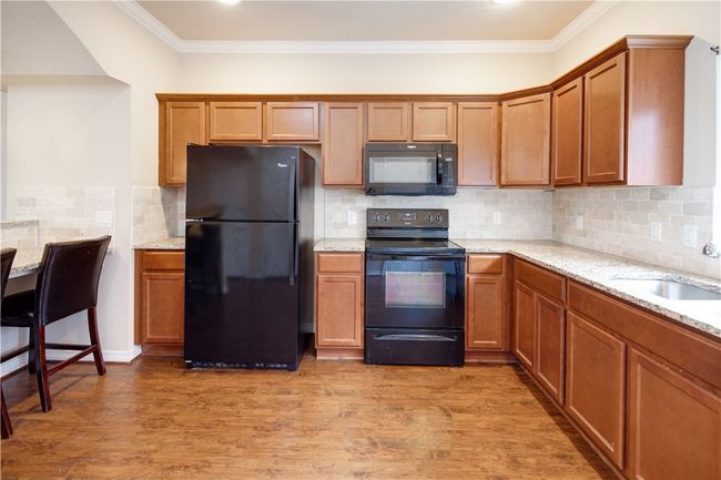 Kitchen featuring a sink, black appliances, brown cabinets, light wood finished floors, and ornamental molding | Image 5