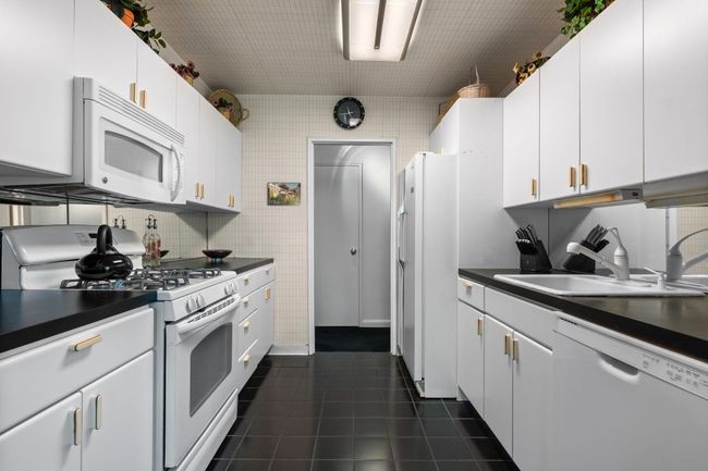 Kitchen with white appliances, dark countertops, dark tile patterned flooring, white cabinetry, and tasteful backsplash | Image 5