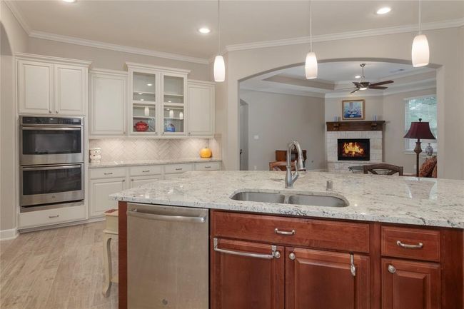 This photo showcases a modern kitchen with an elegant, open layout. It features a double oven, and ample cabinetry. The space flows into a cozy living area with a fireplace, creating a warm and inviting atmosphere. | Image 15