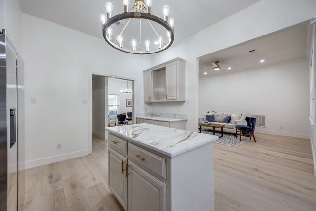 Kitchen with a chandelier, light wood-style flooring, light stone countertops, open floor plan, and a kitchen island | Image 12