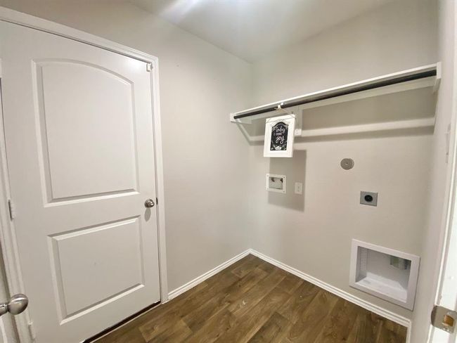 Laundry room with wood flooring, a single door, and hookups for a washer and dryer. There's a shelf for storage and neutral-colored walls, creating a clean and functional space. | Image 10