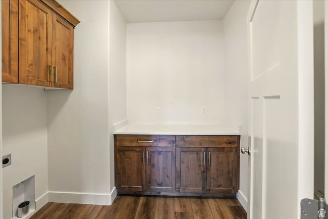 Laundry area featuring electric dryer hookup, dark wood-style flooring, cabinet space, and baseboards | Image 23