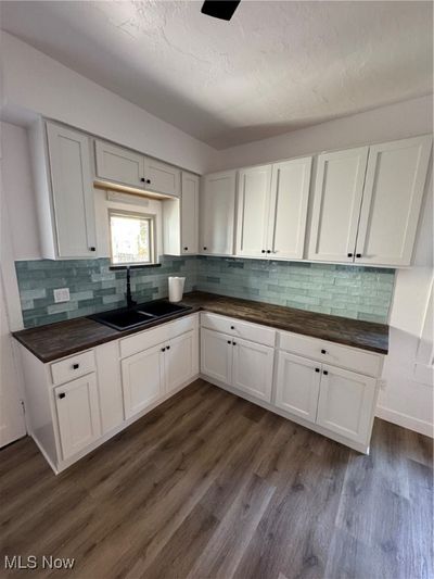 Kitchen with dark hardwood / wood-style floors, decorative backsplash, white cabinetry, and sink | Image 2