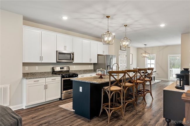 Kitchen with dark hardwood / wood-style flooring, stainless steel appliances, pendant lighting, a center island with sink, and white cabinetry | Image 13