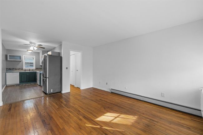 Unfurnished living room with a sink, a ceiling fan, baseboards, baseboard heating, and dark wood finished floors | Image 5