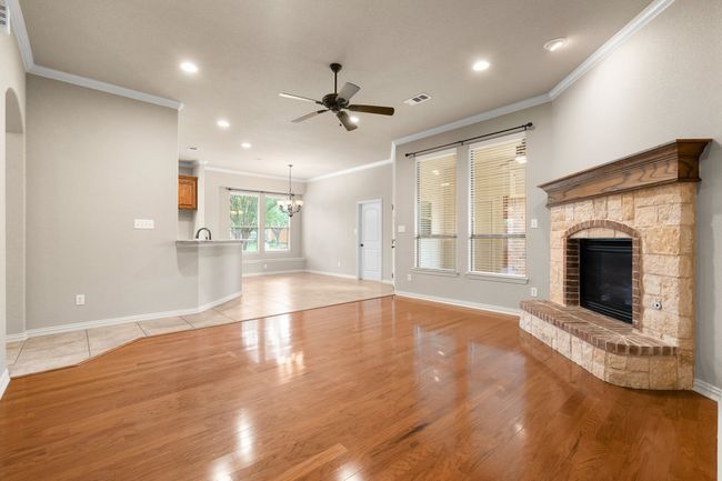 Unfurnished living room featuring ceiling fan, a glass covered fireplace, a chandelier, crown molding, and light wood-type flooring | Image 11
