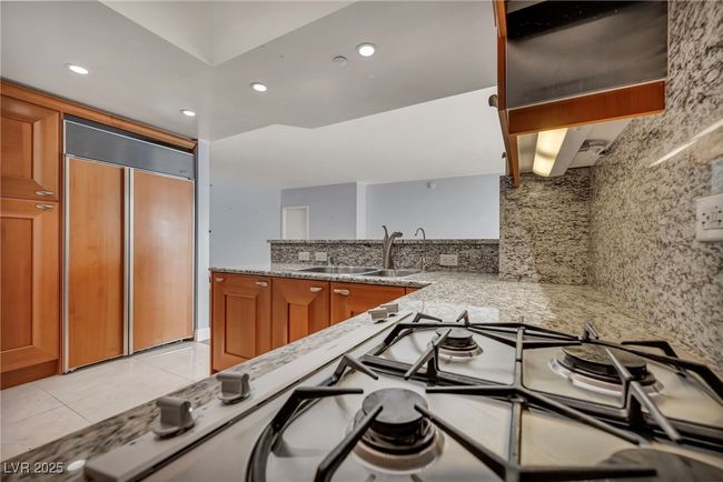 Kitchen featuring brown cabinets, light stone counters, paneled built in fridge, a sink, and decorative backsplash | Image 25
