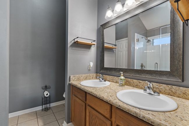 Bathroom with a stall shower, tile patterned floors, toilet, double vanity, and baseboards | Image 15