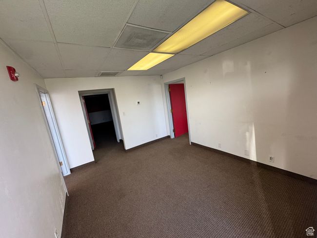 Empty room featuring a paneled ceiling, visible vents, dark colored carpet, and baseboards | Image 6