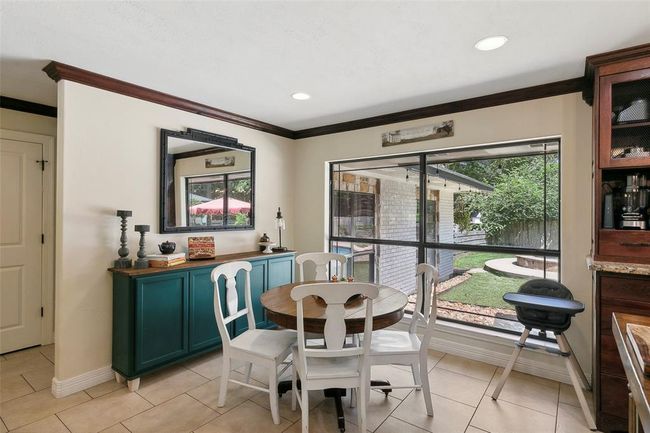 Bright dining area with large windows overlooking the backyard. Features a cozy round table, stylish teal sideboard, and neutral tile flooring, creating a welcoming atmosphere. | Image 17