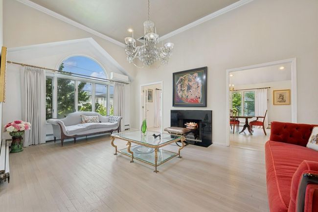 Living area featuring a chandelier, a lit fireplace, crown molding, wood finished floors, and a high ceiling | Image 5