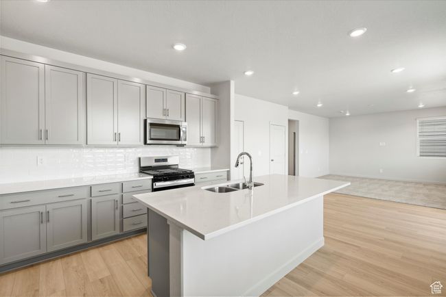 Kitchen featuring appliances with stainless steel finishes, gray cabinets, backsplash, light wood-style floors, and a center island with sink | Image 17