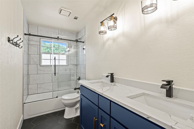 Full bathroom featuring double vanity, tile patterned floors, enclosed tub / shower combo, and a textured wall | Image 25