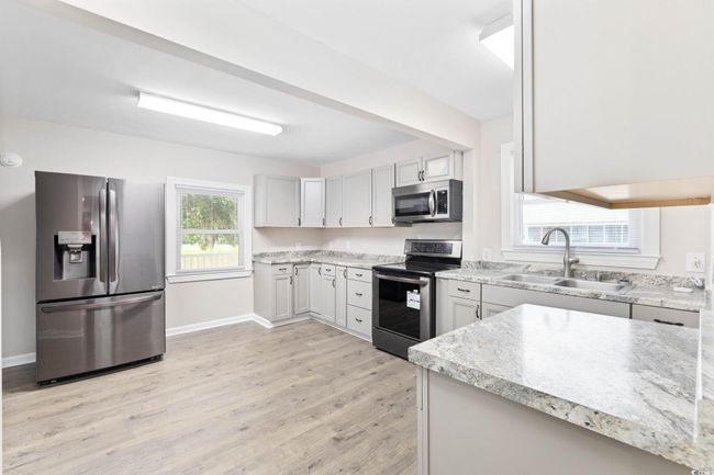 Kitchen featuring stainless steel appliances, a sink, light wood-type flooring, baseboards, and light stone counters | Image 17