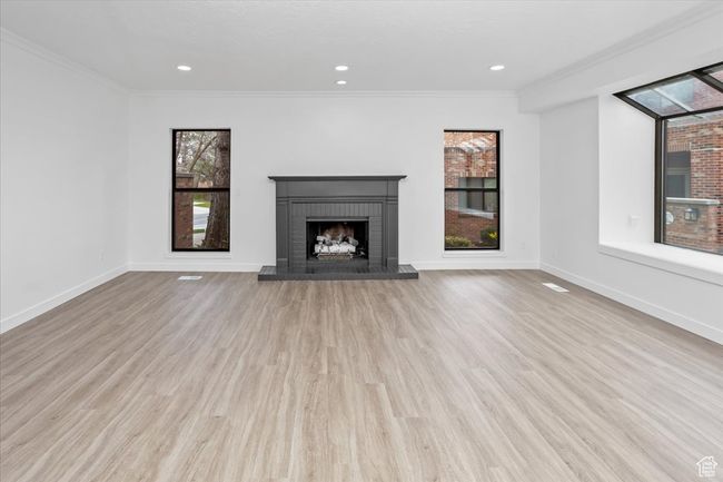 Unfurnished living room featuring a brick fireplace, ornamental molding, baseboards, and wood finished floors | Image 4