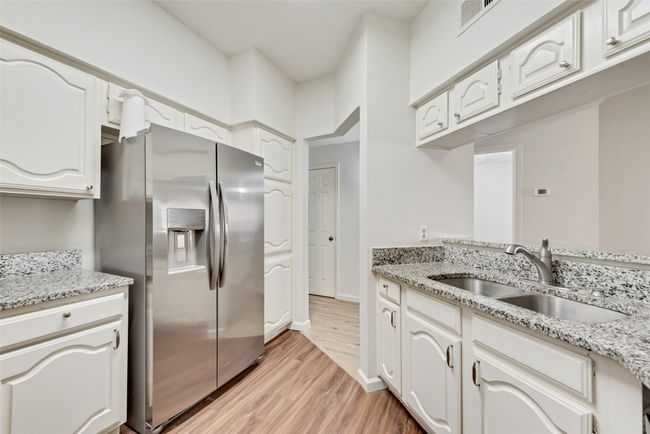 Kitchen with stainless steel fridge, light wood finished floors, light stone counters, and white cabinets | Image 10