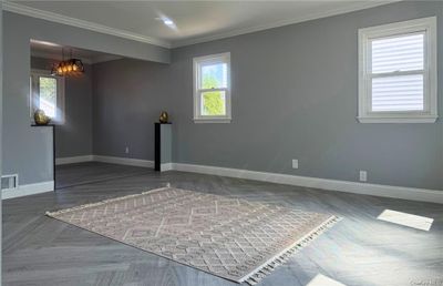 Empty room with a notable chandelier, dark parquet floors, and ornamental molding | Image 3