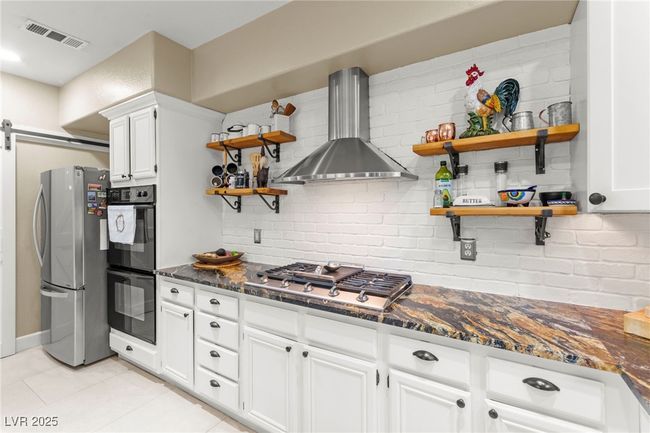 Kitchen with open shelves, appliances with stainless steel finishes, wall chimney exhaust hood, tasteful backsplash, and light tile patterned floors | Image 9
