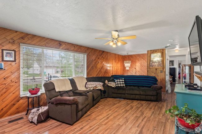 Living room with light wood-style floors, a ceiling fan, wooden walls, and a textured ceiling | Image 5