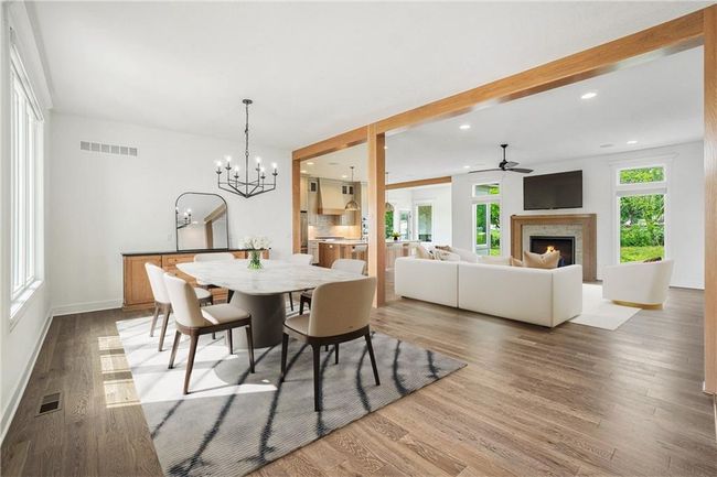 Dining space with a ceiling fan, a lit fireplace, a chandelier, wood finished floors, and baseboards | Image 15