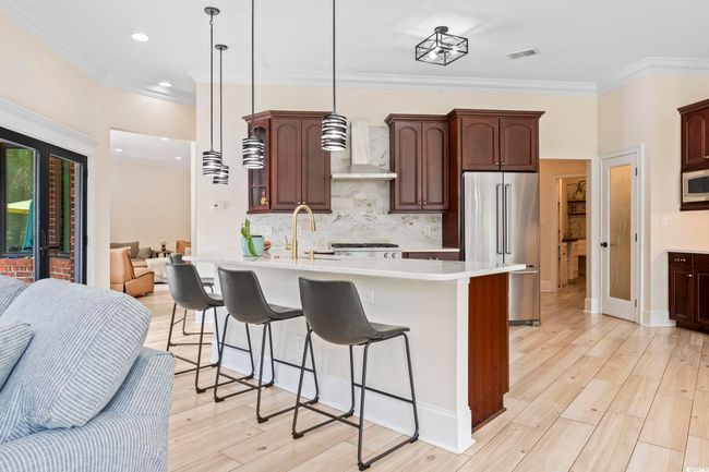 Kitchen featuring high end fridge, wall chimney range hood, a kitchen bar, a sink, and crown molding | Image 9