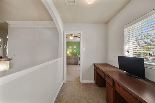 A study overlooking the foyer below connects the third & fourth bedrooms. Features include two wood-stained built-in desks accompanied by a window with blinds above, ceiling mounted lighting & carpet. The fourth bedroom is shown in the background. | Image 35