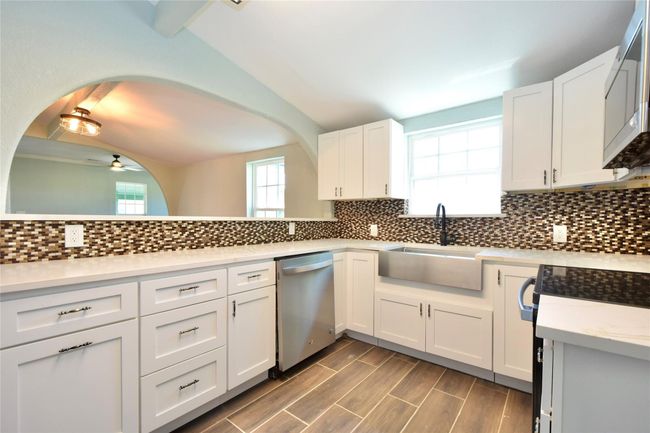 Kitchen featuring stainless steel dishwasher, white cabinets, a ceiling fan, backsplash, and arched walkways | Image 13