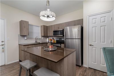 Kitchen featuring appliances with stainless steel finishes, a kitchen island, dark hardwood / wood-style floors, and hanging light fixtures | Image 2