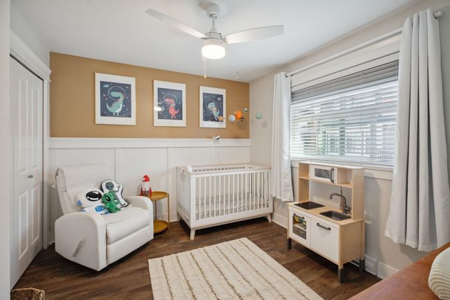 Bedroom with radiator, ceiling fan, dark wood finished floors, a wainscoted wall, and a crib | Image 22