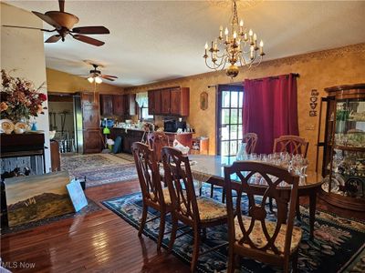 Dining area with lofted ceiling, a textured ceiling, ceiling fan with notable chandelier, and dark hardwood / wood-style flooring | Image 3