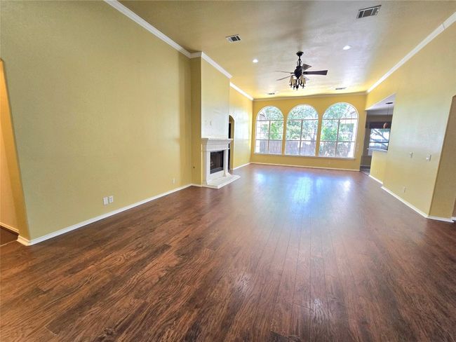 Unfurnished living room with ceiling fan, dark wood finished floors, crown molding, a fireplace with raised hearth, and recessed lighting | Image 9
