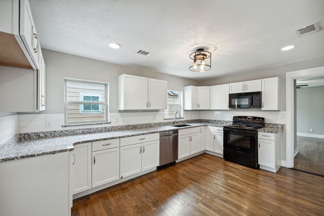 Kitchen featuring black appliances, light stone counters, white cabinets, dark wood-style flooring, and recessed lighting | Image 7