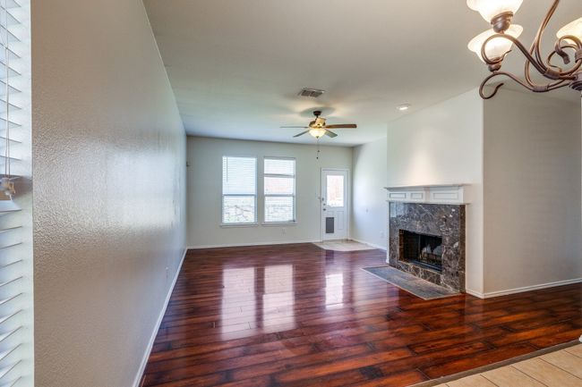 Unfurnished living room with visible vents, baseboards, hardwood / wood-style flooring, ceiling fan with notable chandelier, and a premium fireplace | Image 4
