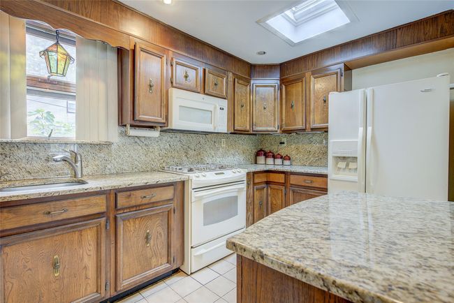Kitchen with white appliances, a skylight, brown cabinets, light tile patterned flooring, and decorative backsplash | Image 15