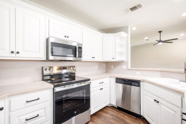 Kitchen featuring stainless steel appliances, dark wood-style floors, white cabinets, light countertops, and a ceiling fan | Image 8
