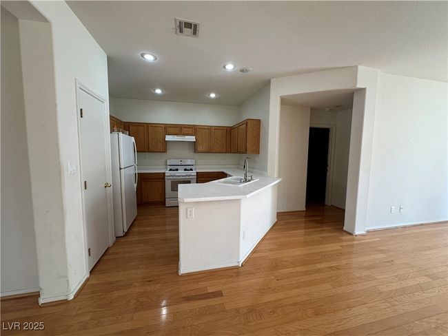 Kitchen with white appliances, a sink, under cabinet range hood, light wood-style floors, and a peninsula | Image 12