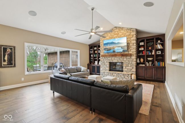 living room with lofted ceiling, visible vents, a ceiling fan, a stone fireplace, and wood finished floors | Image 20