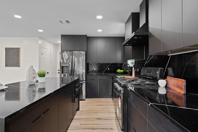 Kitchen featuring range with gas stovetop, stainless steel fridge, wall chimney range hood, light wood-type flooring, and decorative backsplash | Image 11