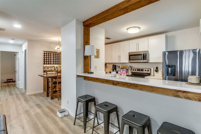 Kitchen featuring light wood-type flooring, a breakfast bar area, stainless steel appliances, white cabinetry, and visible vents | Image 5