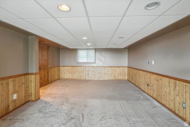 Basement living room featuring a wood wainscoted wall, carpet floors, recessed lighting, and a paneled ceiling | Image 19