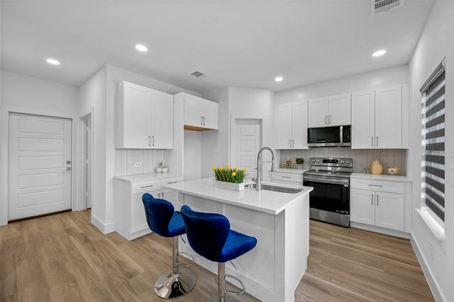 Kitchen with appliances with stainless steel finishes, decorative backsplash, light wood finished floors, light countertops, and white cabinetry | Image 7