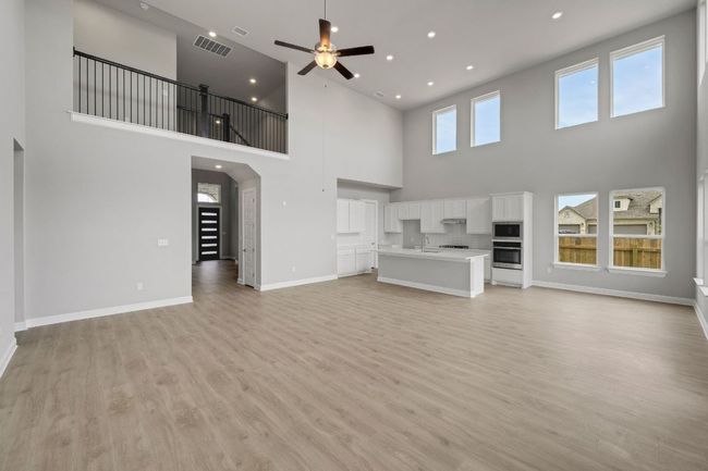Unfurnished living room with light wood finished floors, ceiling fan, arched walkways, recessed lighting, and a towering ceiling | Image 7