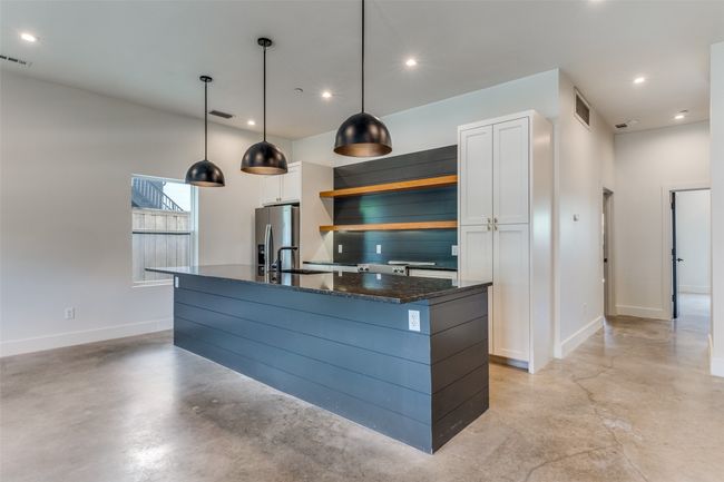 Kitchen featuring concrete flooring, stainless steel fridge, white cabinetry, a center island with sink, and dark stone counters | Image 6
