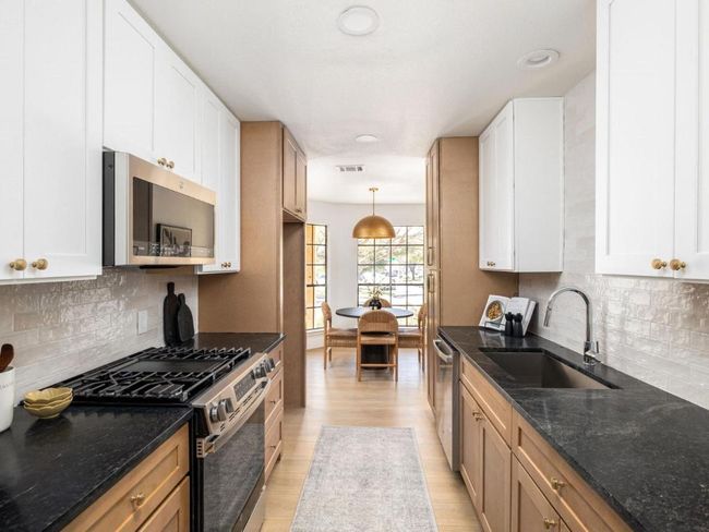Kitchen featuring white cabinets, dark stone counters, appliances with stainless steel finishes, a sink, and light wood-style floors | Image 5