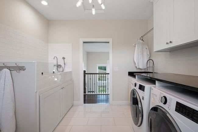 Upper level laundry room is complete with tile floors, LG front-load washer and dryer, a folding table, utility sink, and a handy dog washing station. | Image 24