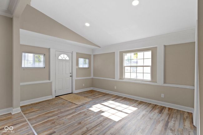 foyer entrance featuring light wood finished floors, vaulted ceiling, recessed lighting, baseboards, and crown molding | Image 9