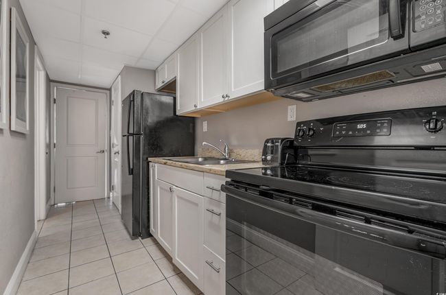 Kitchen featuring black appliances, white cabinetry, light tile patterned flooring, and light stone countertops | Image 5