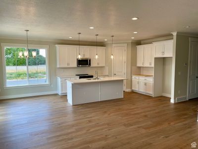 Kitchen featuring decorative light fixtures, a kitchen island with sink, white cabinetry, and light wood-type flooring | Image 2