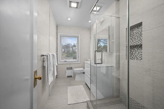 Bathroom featuring tile patterned flooring, tile walls, toilet, a shower stall, and radiator heating unit | Image 15